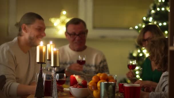 Dostu aile Noel akşam yemeği için toplandı. Masanın üstünde mumlar, meyve, mandalina, şarap var. Herkes animatedly konuşuyor, şaka, yemek — Stok video
