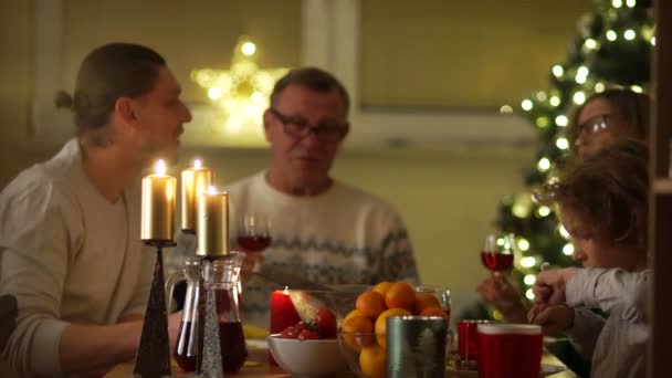 Tradición familiar, recepción de Navidad. Abuela y abuelo invitaron a los niños y nietos a visitar. Las personas mayores se besan mientras están sentadas en la mesa de la familia — Vídeos de Stock