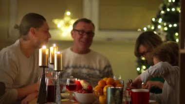 Dekore edilmiş bir Noel ağacı arka plan üzerinde mum ışığında aile Noel yemeği. Genç bir kadın kızarmış tavuk getirdim. Büyükbaba, Büyükanne, oğlu ve torunu çok mutluyuz