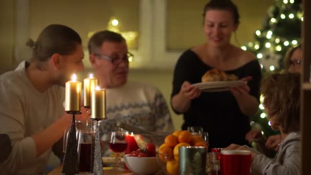 Eine junge Familie verwöhnt ihre Eltern am Tisch. junge Frau kochte Hühnchen. Weihnachten bei Kerzenschein, glückliche Familie — Stockvideo
