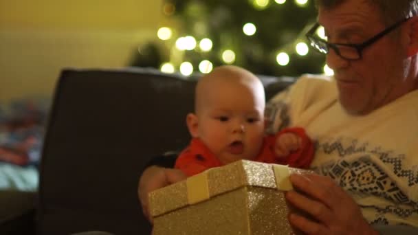 祖父と孫のクリスマス プレゼント ボックスを開きます。新しい年の前夜に彼の祖父の膝の上の赤ちゃん — ストック動画