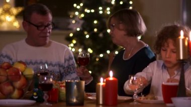 Noel masa mum ışığında çok güzel aile. Büyükanne ve büyükbaba gözlük, şarap içmek kıvırcık torunu Salata yiyor. Mutlu Noeller