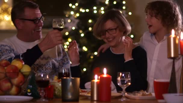 Ein älteres Ehepaar mit seinem Enkel am Weihnachtstisch in der Abenddämmerung. eine Frau freut sich, lächelt, singt