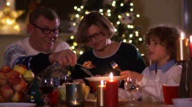 Mutlu bir aile kutlama Noel yılbaşı ışıkları çerçevede mum ışığında. Büyükbaba onun torunları plaka salata koyar. Vejetaryen yemek