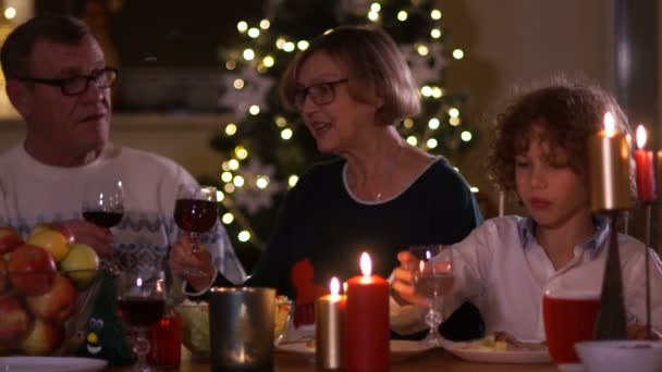 Großvater und Großmutter trinken Rotwein, während sie am Festtagstisch sitzen. Weihnachtstoast, Weihnachtswünsche, glückliche Familie
