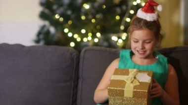 Bir zarif yeşil elbise ve kafa bandı Noel Baba şapkası ile kız öğrenci bir hediye açılır. Kız çok şaşırdım ve memnun, çocuk Noel ağacı yakınındaki kanepede oturuyor