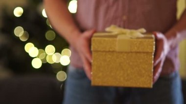 Mens eller bir kurdele ile bağlanmış bir hediye ile altın bir kutu germek. Yakın çekim Noel hediyesi