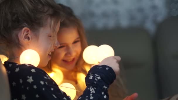 Zwei Freundinnen der Schülerin spielen abends zu Hause mit leuchtenden Girlanden. Hausbeleuchtung, mädchenhafte Freundschaft, Pyjama-Party — Stockvideo