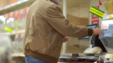 Sakallı gri saçlı emekli bir süpermarkette ölçeklerde hububat ağırlığında, bir paket üzerinde bir fiyat etiketi sopa. Yalnız yaşlı adam, bakkal bölümü