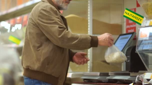 Gepensioneerde m/v met een gewicht van graan op de weegschaal in de supermarkt. Eenzame oude man, kruidenier departement — Stockvideo
