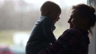 Siluetleri genç bir anne ve bir altı - ay önce çocuğun pencerenin arka planı. Doğum izni üzerinde ev kadını anneler günü