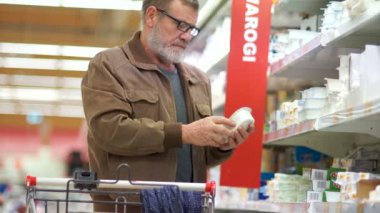 Gri sakallı bir yalnız adam süzme peynir süpermarket süt bölümünden seçer.