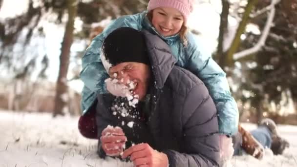 Ragazza gioca palle di neve con suo padre, sono sdraiati nella neve e ridendo allegramente. Buone vacanze in famiglia — Video Stock