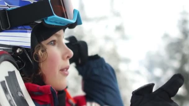 Um retrato próximo. O adolescente de capacete e óculos ergue-se numa cabana de ski lift. A criança ri alegremente. Férias divertidas nas montanhas, estilo de vida ativo — Vídeo de Stock