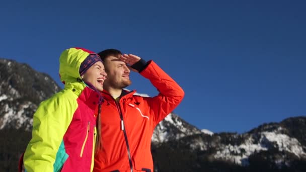 El tipo y la chica de vacaciones en una estación de esquí. Pareja mira a la distancia, poniendo sus manos en la frente, acercándose desde el sol — Vídeo de stock