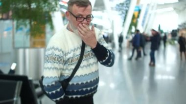 Örme kazak ve gözlük havaalanında gri sakallı adam olgun ya da tren istasyonu. Emekli elveda dalgalar ve onun arkasında tekerlekli bavul taşıma bırakır