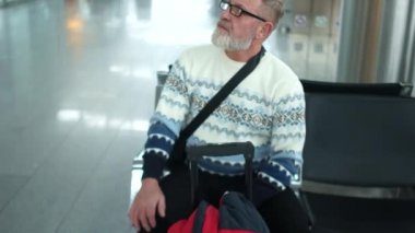 Olgun çekici adam beyaz kazak ve gözlük Havaalanı dinlenme odasında oturuyor. Onun uçuş açıkladılar, ayağa kalkar ve iniş bavulla bırakır