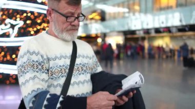 Adam uluslararası havaalanında uçuş varış için bekliyor. Halen bir pasaport ve Noel ağacı arka plan üzerinde duran bir bilet tutuyor