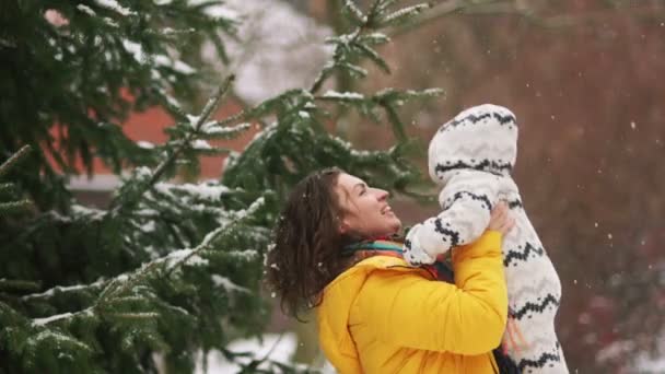 Baby på en promenad i armarna på sin mor. Vinter promenad i parken under snön. Mor kastar baby upp, baby ser förvånad — Stockvideo