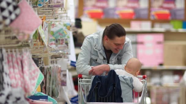 成熟した父は、スーパー マーケットのカートに自分の赤ちゃんを置くし、彼女が買い物をする間、彼の妻のため待機します。父の日 — ストック動画