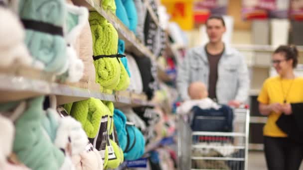 Family of three in the supermarket. Mother father and baby in supermarket trolley choose fleece light green blanket — Stock Video