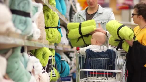 Keluarga bahagia dengan bayi membeli selimut bulu selada di supermarket. Anak itu menarik tangan untuk pembelian cerah — Stok Video