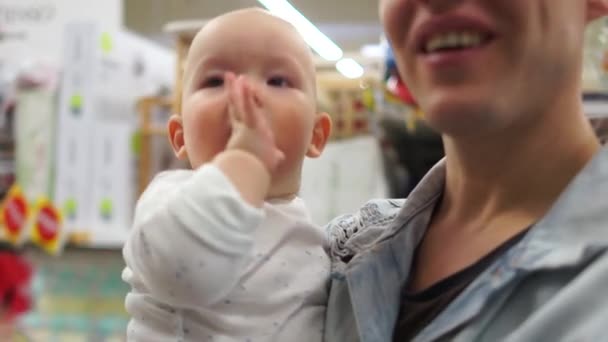 Papà e il suo figlioletto stanno scegliendo un giocattolo. La bambina si rallegra del sonaglio e glielo tira in bocca. Emozioni bambino di anni. Giorno di padri — Video Stock