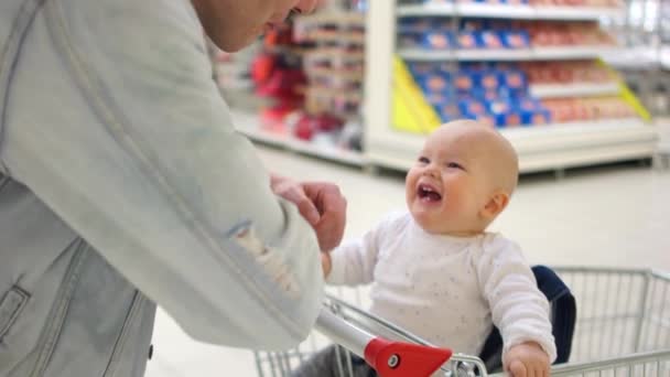 父とスーパー マーケットで彼の小さな赤ちゃん。子供はカートに座っているし、大喜びで彼の父を見ています。男は、彼に話しています。父の日 — ストック動画