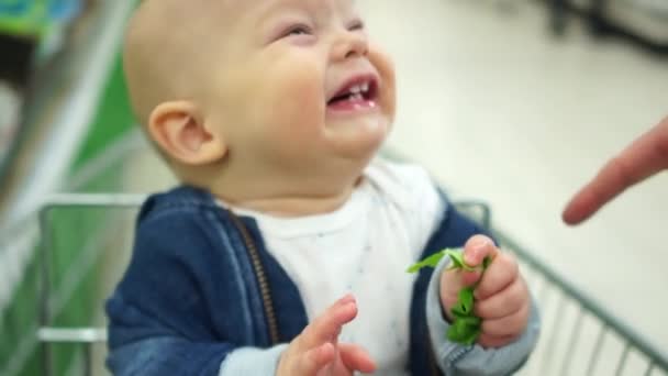 かわいい赤ちゃんは、スーパー マーケットのトロリーに座っている完全な口を笑います。彼の最初の乳歯が表示されます。父笑子供、子供の感情 — ストック動画