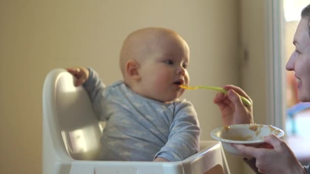 Mamma matar sin roliga son från en sked med äppelmos. Baby böjda och vände sig bort — Stockvideo