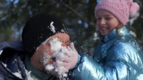 En pige smører sne på sin fars ansigt. Mand griner. Alvorlig sne kamp – Stock-video