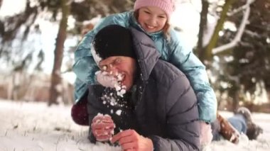 Kız, babasıyla kartopu oynuyor, karda yalan ve neşeyle gülerek. Mutlu aile tatilleri