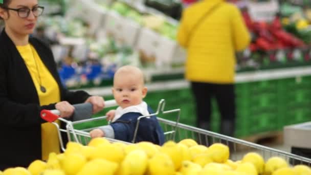 Fiatal anya, baba, vásárlás a szupermarketben. A gyermek ránéz citrom örömében, gyerekek fejlesztése — Stock videók