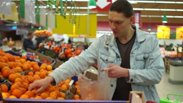 Joven con un carrito de supermercado comprando mandarinas para niños. Alimento saludable — Vídeos de Stock