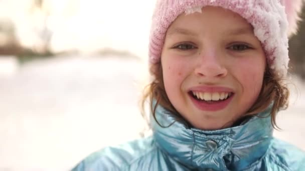 Close portrait of a girl in a snowy pink hat after a snow fight in the park. The child smiles cheerfully — Stock Video