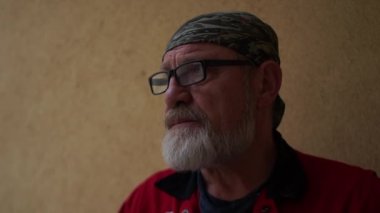 Yakışıklı adam gri sakal ve gözlük bir sigara içiyor ve mesafe içine düşünceli görünüyor. Onun kafa bandı. Portre kadar kapatın