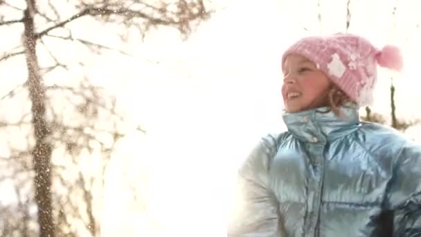 Chica sonriente disfrutando de la fría y soleada mañana en el parque. Alegre colegiala activa está lanzando bola de nieve a la cámara divertirse al aire libre durante el invierno — Vídeos de Stock