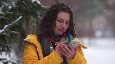 Kıvırcık kumral kartopu oyunu sırasında parkta. Ne zaman bir kartopu gets kız telefon tutar. Kış oyunları, Bayramınız kutlu olsun