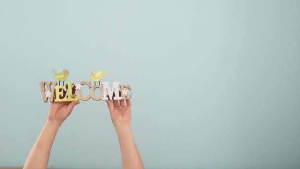 Fotografía de primavera y Pascua en el estudio. Las manos del bebé sobre un fondo azul sostienen y balancean letreros de madera con inscripciones Welcome y Spring. El comienzo de la primavera — Vídeo de stock