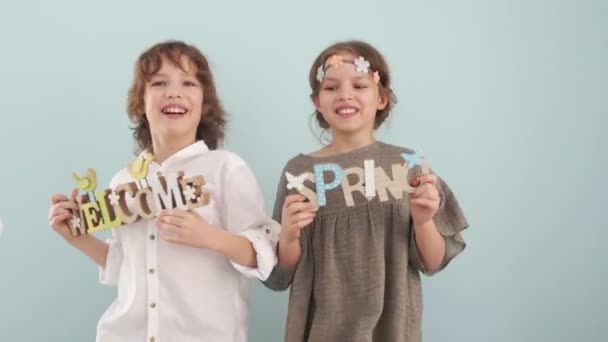 Glad påsk. Söt blå-eyed barn håll trä inskriptioner Välkommen och våren. Barn dans och hoppa, möte våren — Stockvideo