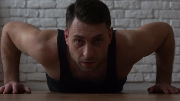 Man took an emphasis lying down and is ready to start pushing up from the floor. Young athlete in the bar, a beautiful blue-eyed brunette with muscular arms — Stock Video