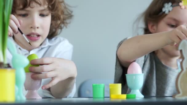 兄と妹は、イースターの装飾の背景に卵をペイントします。小さな男の子と女の子の子供 - イースターのお祝いの準備をしています。 — ストック動画