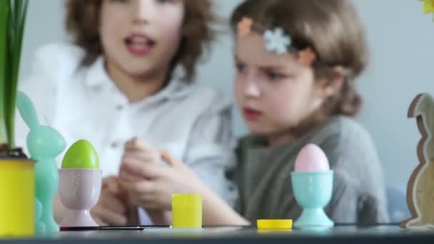 Clase magistral de decoración de Pascua. Chico y chica luchan con borlas, bromas infantiles, pintura verde y amarilla — Vídeos de Stock