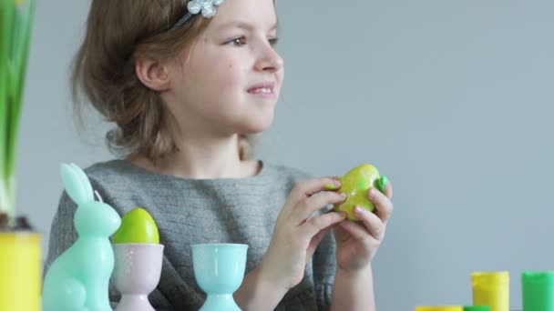 Κορίτσι βάφει τα αυγά του Πάσχα με τα δάχτυλά της. Εικαστική θεραπεία. Χαριτωμένο μαθήτρια σε ένα στεφάνι που κρατά στα χέρια της ένα ελαφρύ πράσινο αυγό του Πάσχα με το fresh paint — Αρχείο Βίντεο