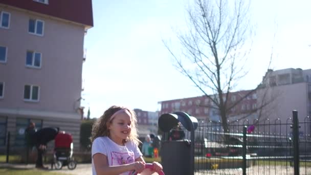 Curly menina passeios de estudante em um balanço rosa alta saltando e gritando com prazer. Movimento lento — Vídeo de Stock
