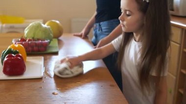 Uzun saçlı kız okul öncesi bir tablo bir havluyla siliyor. Anne ve küçük kızı mutfakta. Anneler asistanı. Kız eğitim