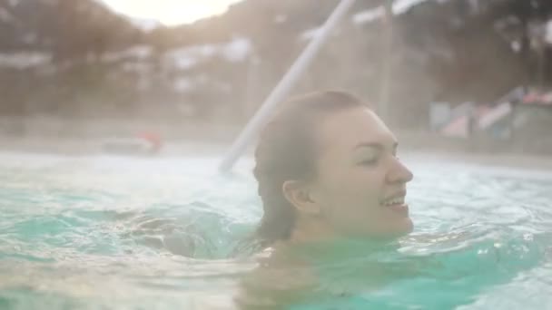 Молодая женщина плавает в горячем источнике на открытом воздухе зимой. Портрет брюнетки и бассейна на холоде — стоковое видео
