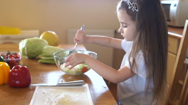 Preschooler s dlouhými vlasy lžíce salát mísy a úsměvů. Maminky pomocník v kuchyni — Stock video