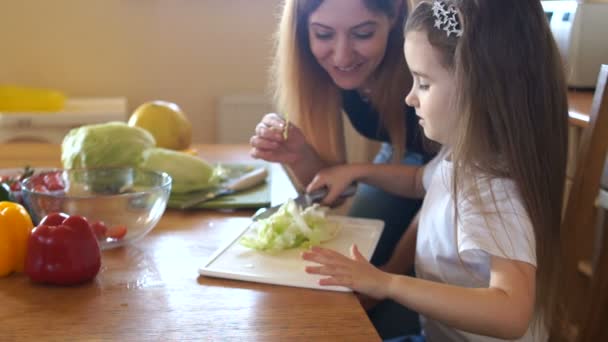 Fille avec maman dans la cuisine. Une fille aide sa mère à préparer une salade. Une femme essaie le chou. Salade verte végétarienne — Video
