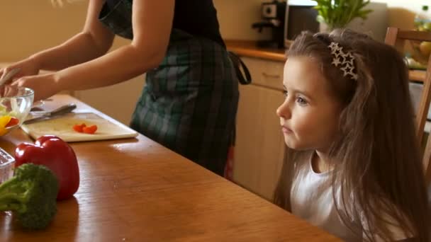 Mother feeds her daughter a healthy lunch in the kitchen. The child is chewing cherry tomatoes, the mother is happy to watch her — Stock Video